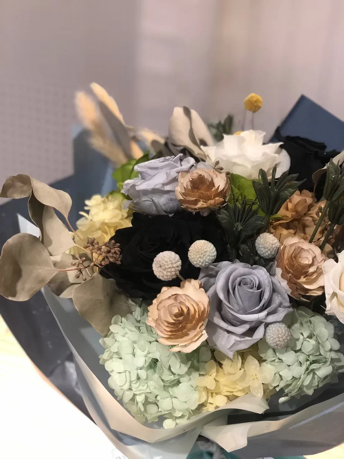 一束用黑白包裝紙包覆的混合花束,包含淡紫色玫瑰、咖啡色玫瑰、白色花朵、淡綠色繡球、乾燥花材和白色球形小花